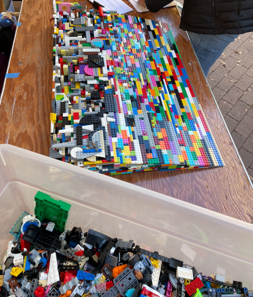 On top of a table we have the semi completed lego ramp with a bucket of legos on its left hand side