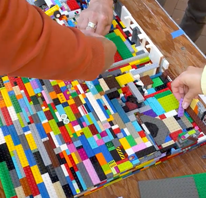 Multiple hands all building a lego ramp on a table.